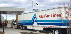 A large moving van is backed up under a portico entrance. Several people are standing at the back of the truck among boxes.