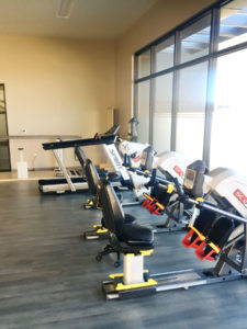 Therapy equipment at Cascadia of Boise, Idaho. Recumbent bikes, a treadmill and parallel bars are lined up facing large windows in a therapy room.